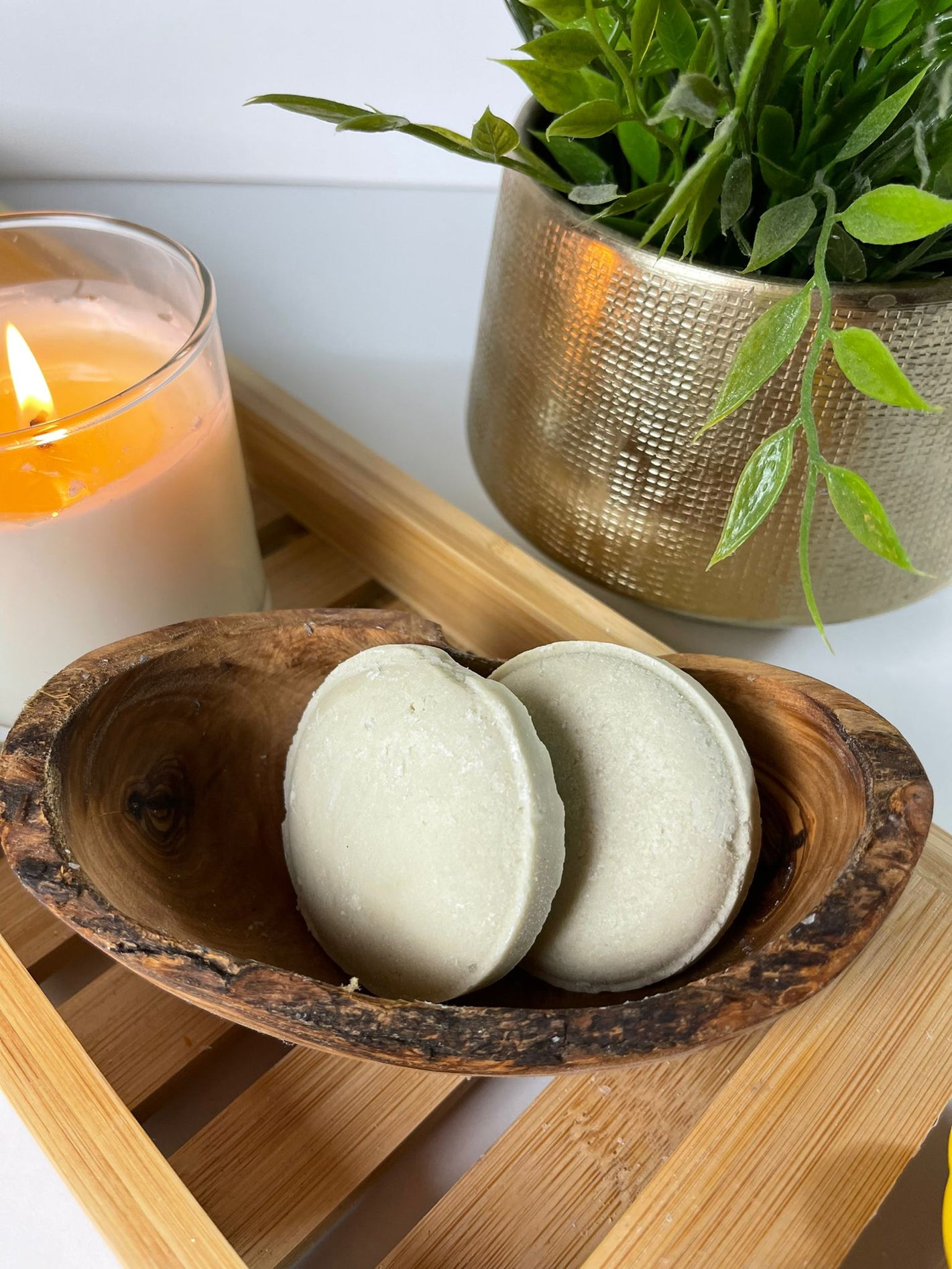 image of two shampoo bars in a woodens soap dish with a burning candle beside them and a plant in the background